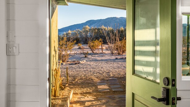 Una puerta que da a un patio con suelo estampado y vistas a un paisaje árido con vegetación escasa y montañas a lo lejos.