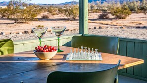 Una mesa con un tablero de ajedrez, un cuenco de uvas y dos copas de martini, ubicada al aire libre frente a un paisaje desértico.