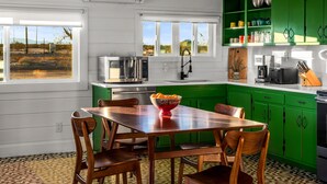 Una cocina moderna con armarios verdes, una mesa de comedor de madera con sillas, un microondas y un ventanal grande.