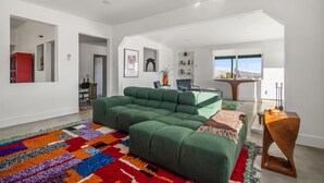 Una sala de estar moderna con un sofá seccional verde, un tapete colorido y vistas al exterior.