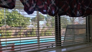 Una ventana con persianas, vista a una piscina y una valla de madera.