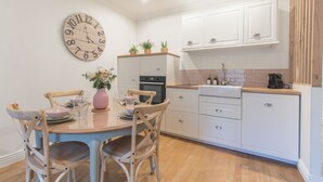 Una cocina con armarios blancos, un reloj de madera y una mesa de comedor con sillas.