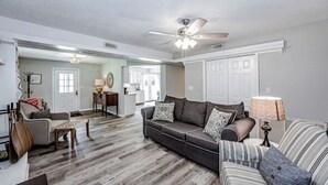 A spacious living room with a grey sofa, a striped armchair, and a wooden coffee table. A ceiling fan is visible, and the room has a hardwood floor. - Tatum’s Retreat -SAUNA- Hiking-Wineries- Unit B (Madison)