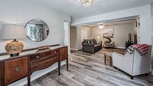 A spacious living room with a wooden floor, a round mirror, a dark-colored sofa, and a white armchair. - Tatum’s Retreat -SAUNA- Hiking-Wineries- Unit B (Madison)