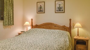 Un lit bien fait, recouvert d’une couvre-lit à motifs, avec deux lampes de chevet et deux tableaux encadrés accrochés au mur.