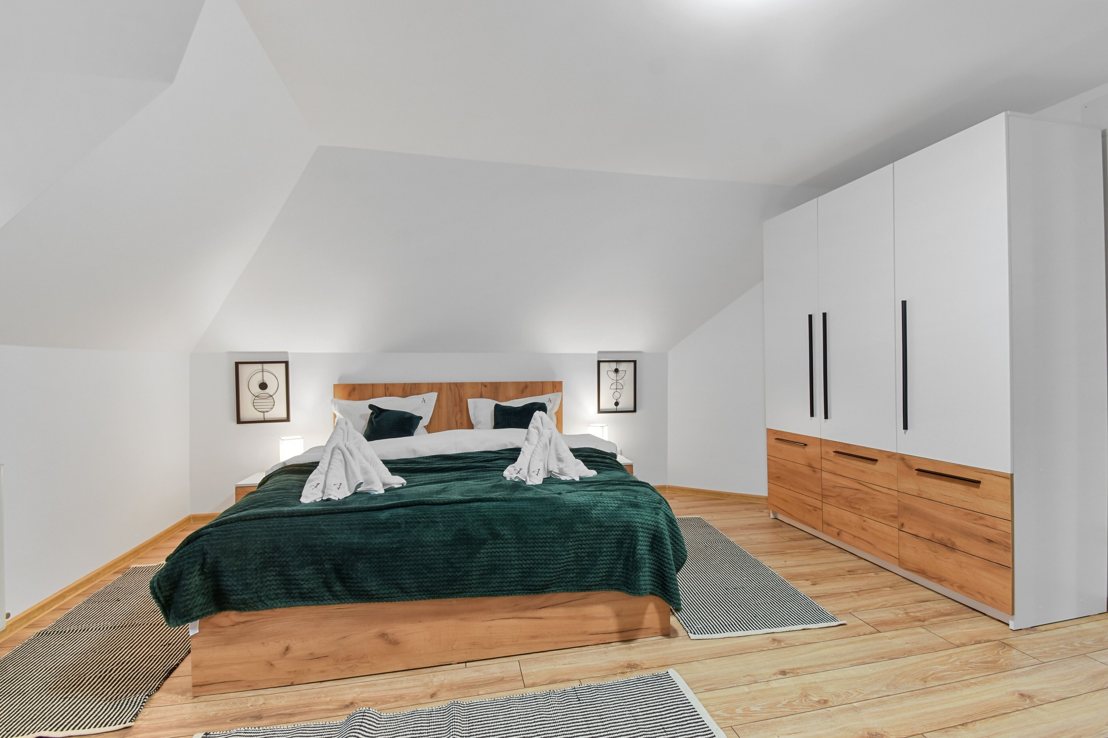 Une chambre à coucher avec un lit, une tête de lit en bois, une armoire blanche et un plafond en pente.