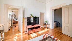 A living room with a TV on a wooden stand, a small table with a plant, and a door leading to another room. - Historic Downtown Loft, Private Deck with View and outdoor Firepit (Lynchburg)