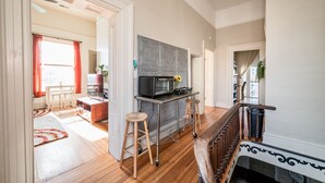 A spacious living area with a wooden floor, a kitchen with a microwave, and a staircase with ornate railings. - Historic Downtown Loft, Private Deck with View and outdoor Firepit (Lynchburg)
