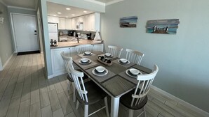 A dining area with a table set for six, white chairs, and a kitchen in the background. - Stunning Views from this lovely 2 bed/2bath (Galveston)