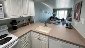 A modern kitchen with white cabinets, a built-in stove, and a dishwasher. There is a dining area with a table and chairs visible in the background. - Stunning Views from this lovely 2 bed/2bath (Galveston)
