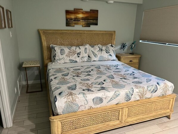 A bedroom with a bed, a nightstand, a wall-mounted artwork, and a window with blinds.