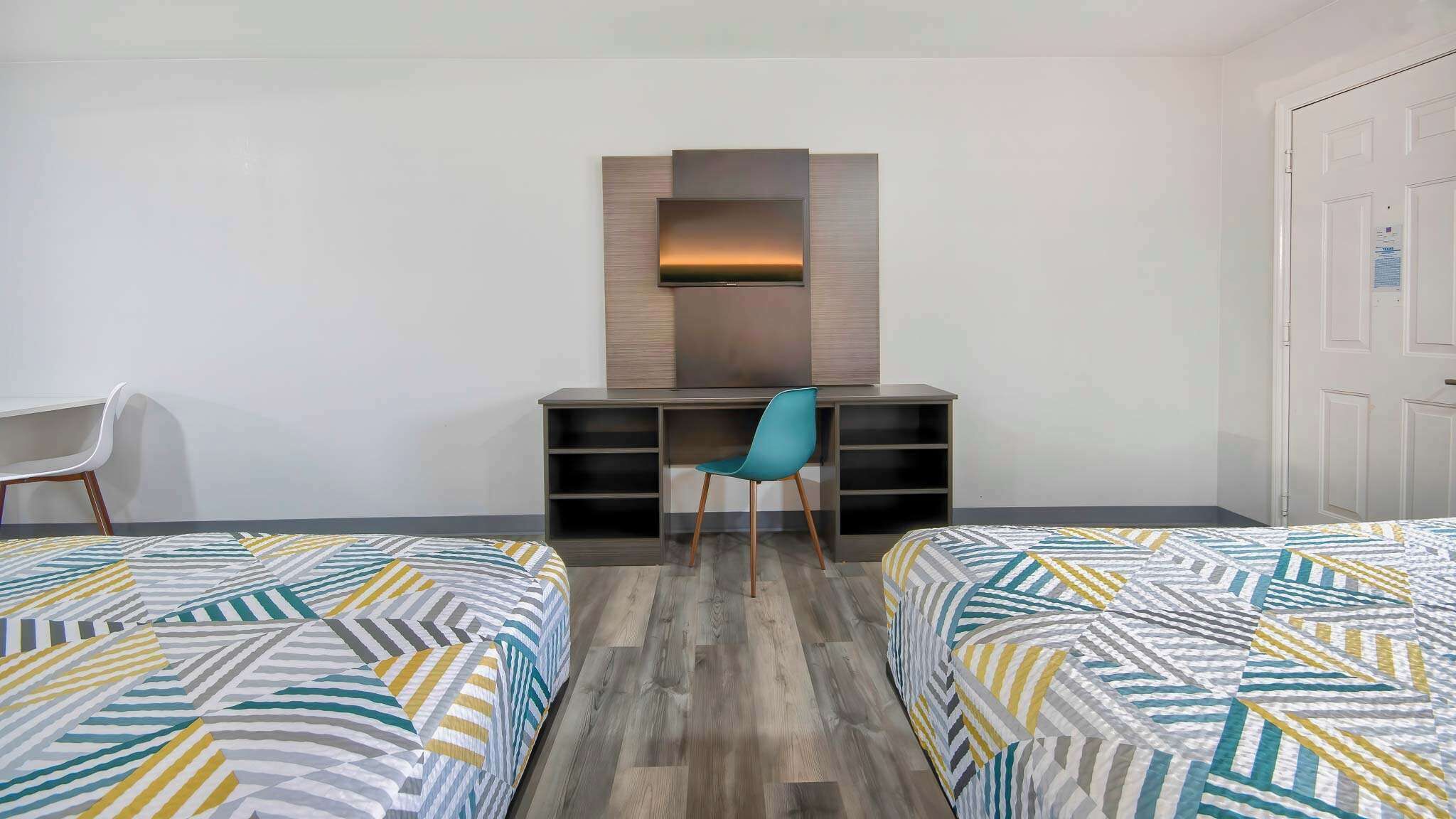 A hotel room with two beds, a desk with a chair, and a TV mounted on the wall.