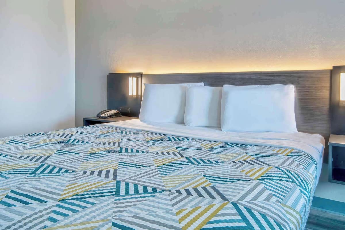 A hotel room with a large bed, a bedside table with a lamp, and a nightstand with a phone.