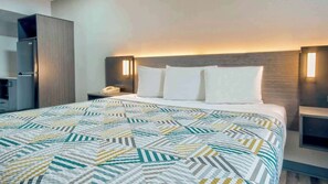 A hotel room with a bed, a nightstand, a telephone, and a minibar. - Studio 6 Texarkana, Tx (Texarkana)