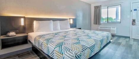 A modern hotel room with a large bed, bedside tables, a desk, and a window with curtains.