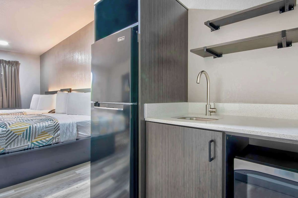 A modern hotel room with a bed, a kitchenette, and a bathroom.