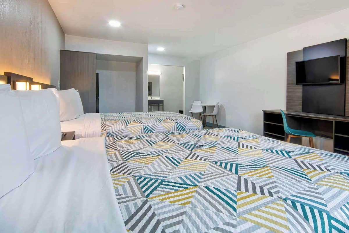 A modern hotel room with a large bed, a desk, a TV, and a mirror.