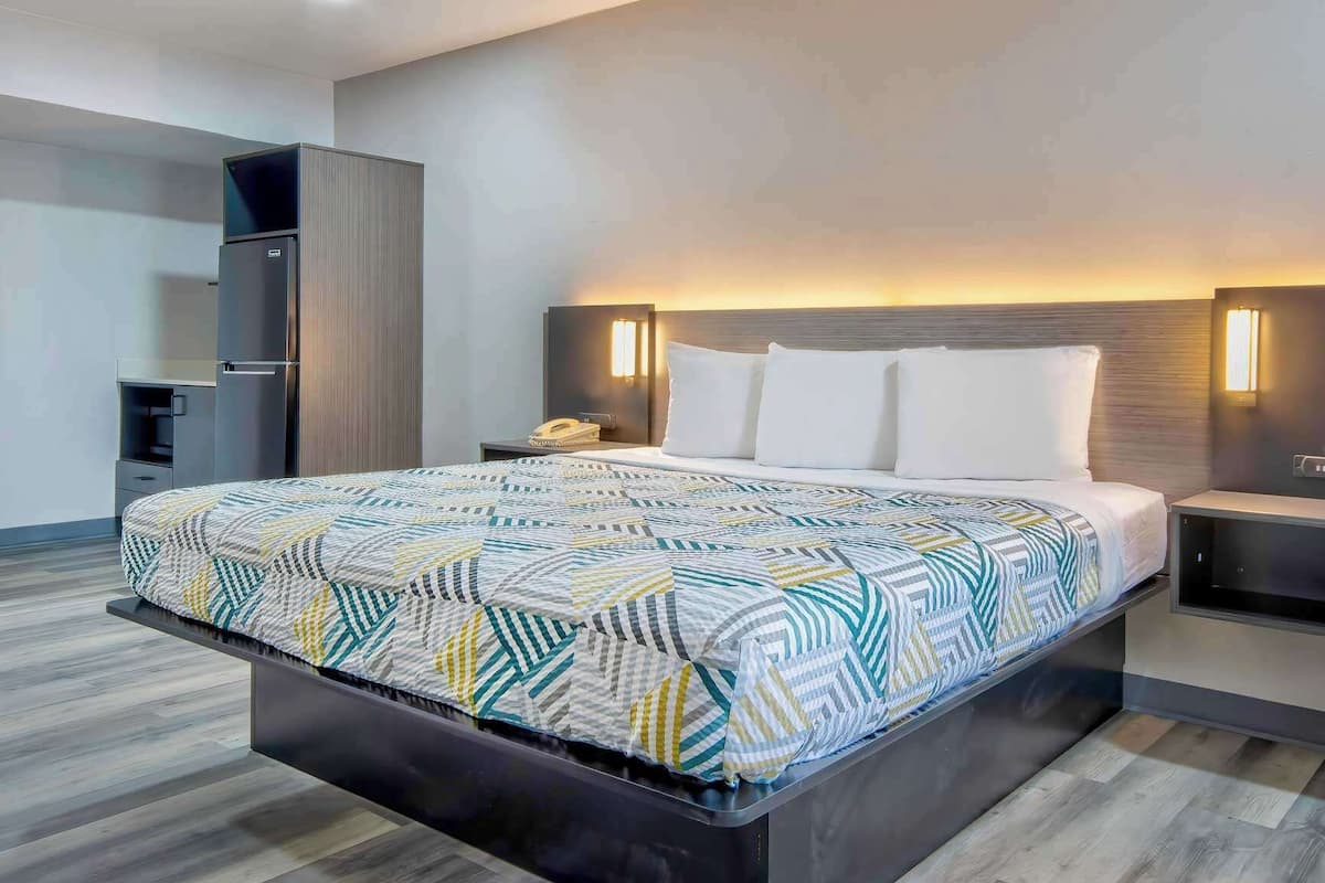 A modern hotel room with a large bed, a built-in wardrobe, bedside tables with lamps, and a wooden floor.