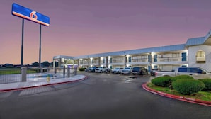 Un motel con un letrero grande, varios espacios de estacionamiento y una entrada con portón.