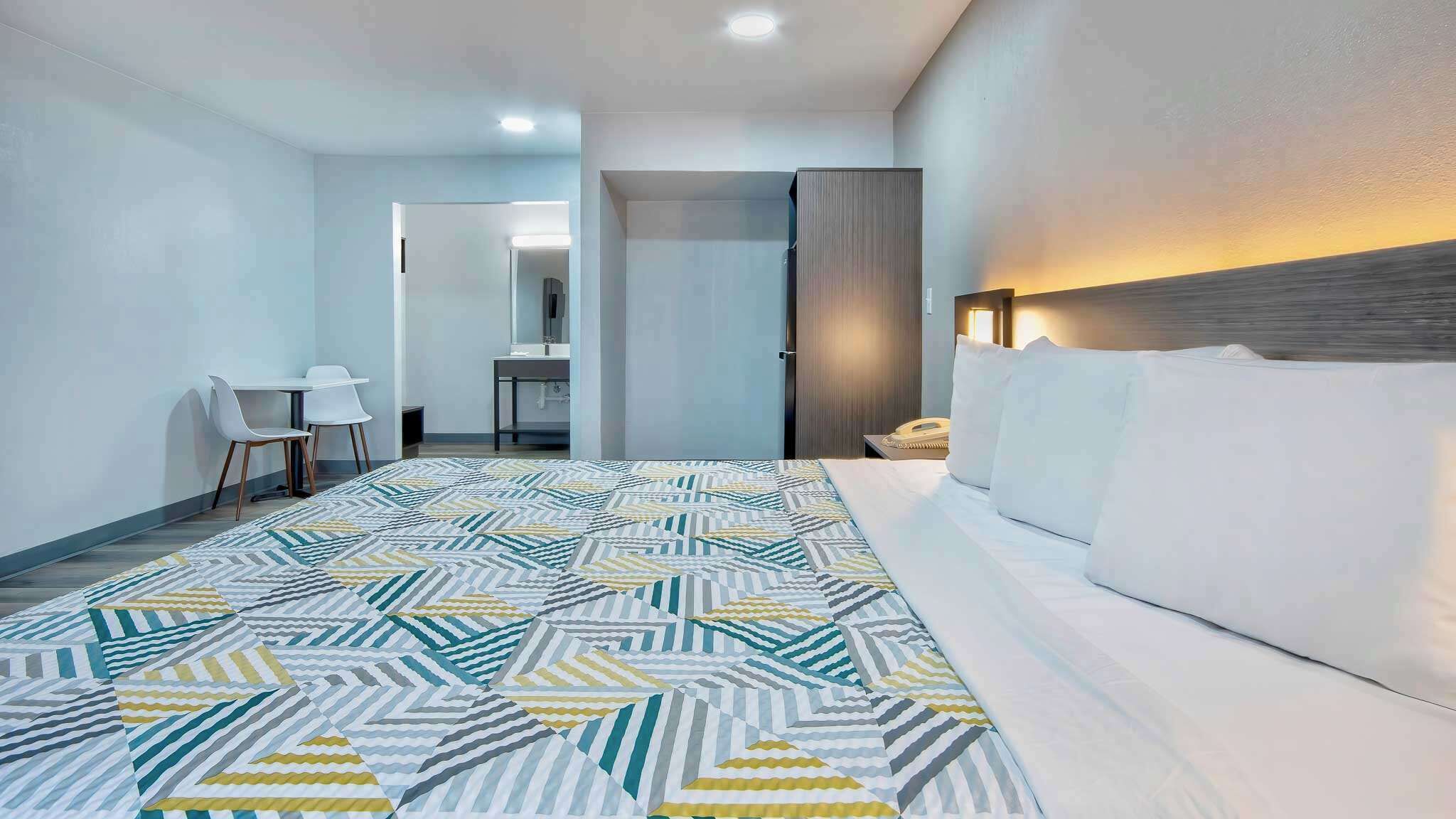 A hotel room with a bed, a desk, a chair, and a bathroom visible through an open door.