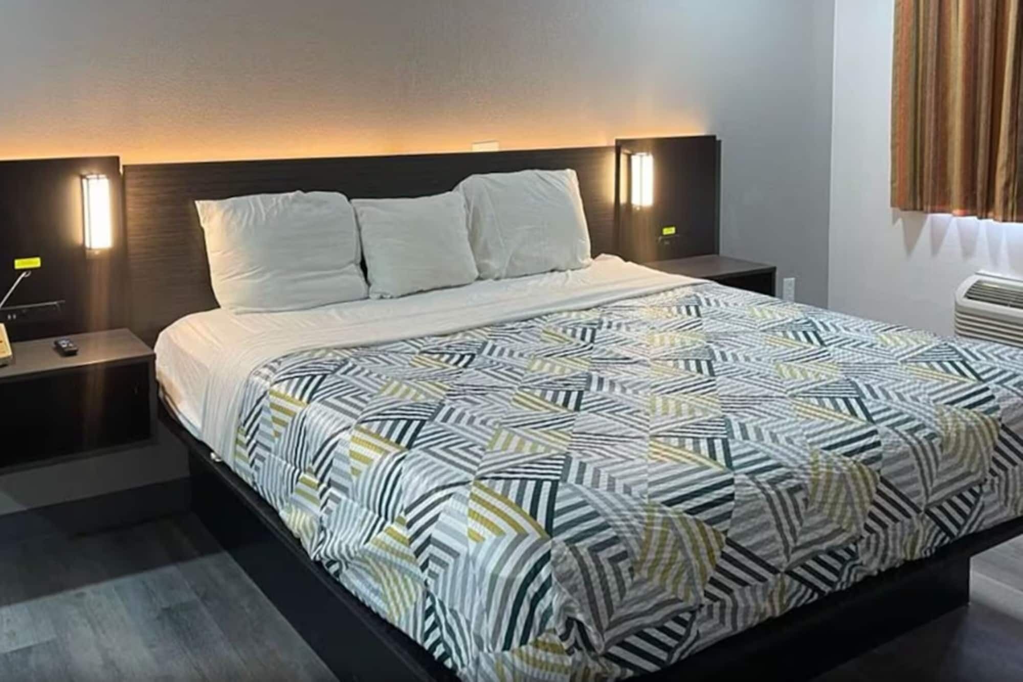 A modern hotel room with a large bed, two bedside tables, and a headboard with integrated lighting.