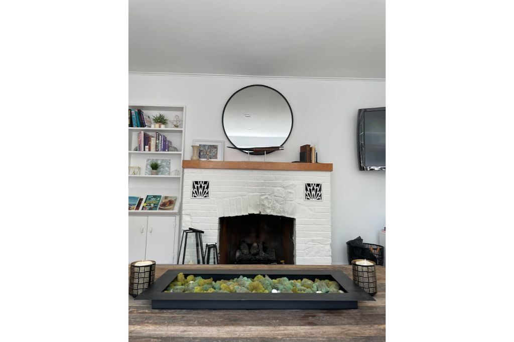 A fireplace with a white brick surround, a mirror above it, and a shelf with books and decorative items.