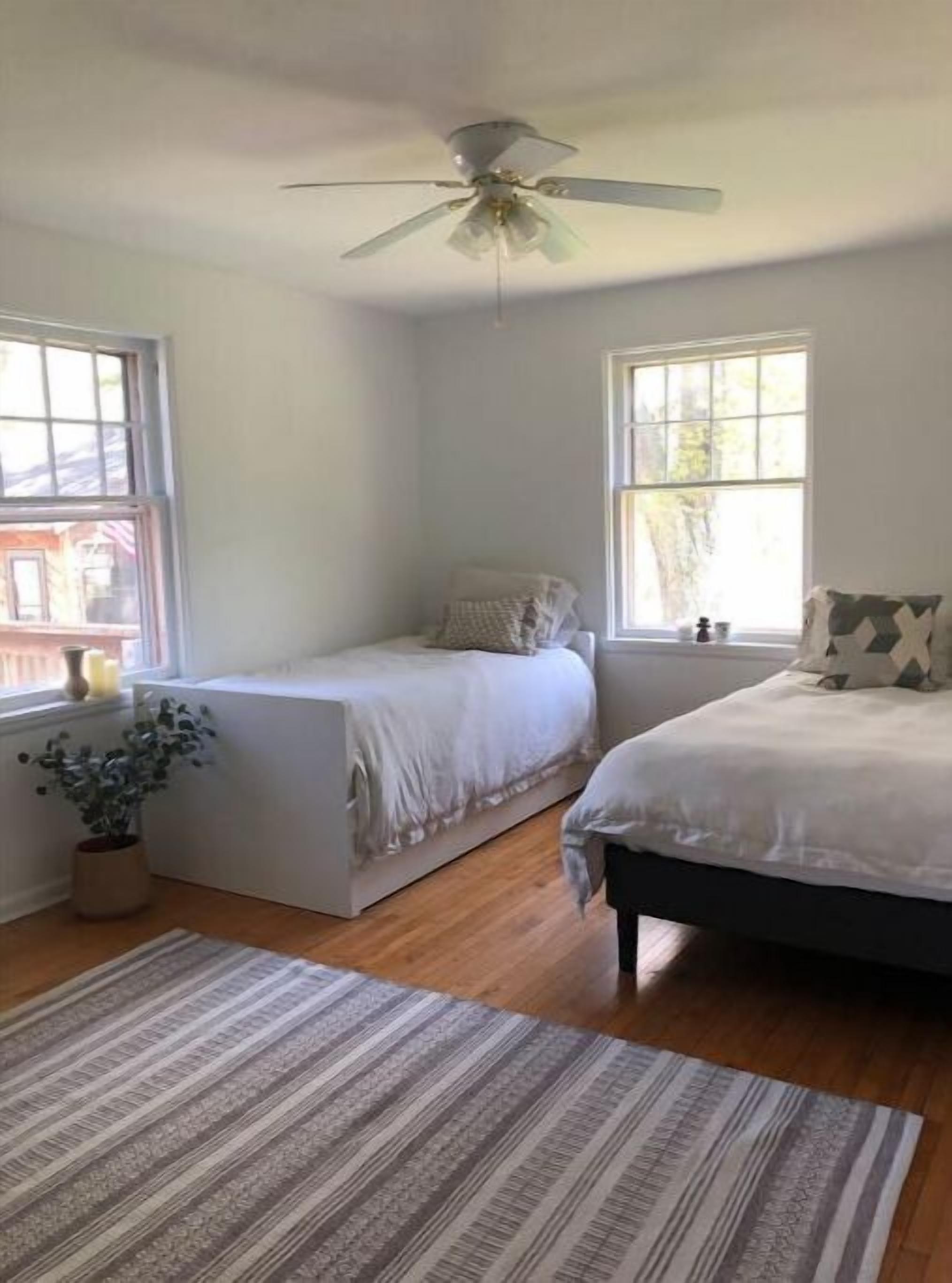 A bedroom with a bed, a small bedside table, a ceiling fan, and a window.
