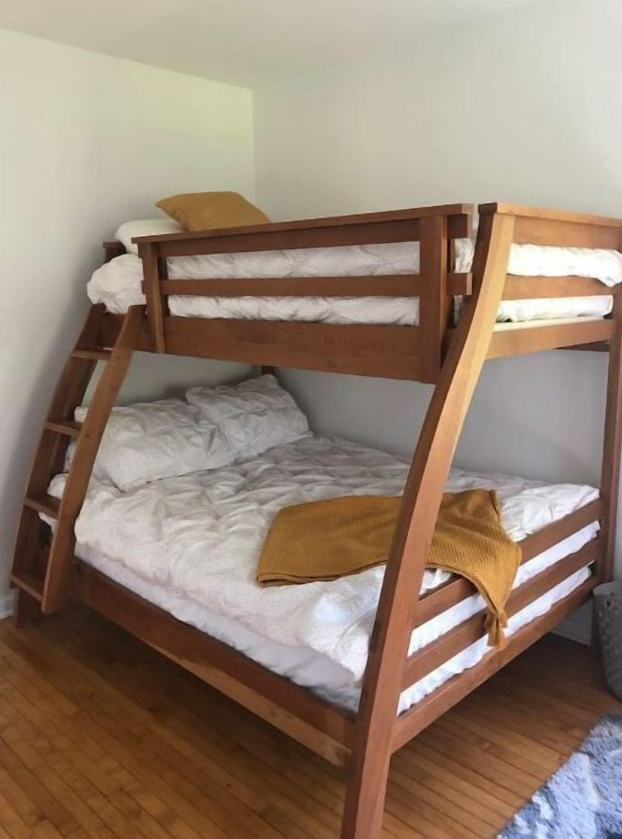 Ein Stockbett mit weißer Bettwäsche und einer Senfgelb-farbenen Tagesdecke.