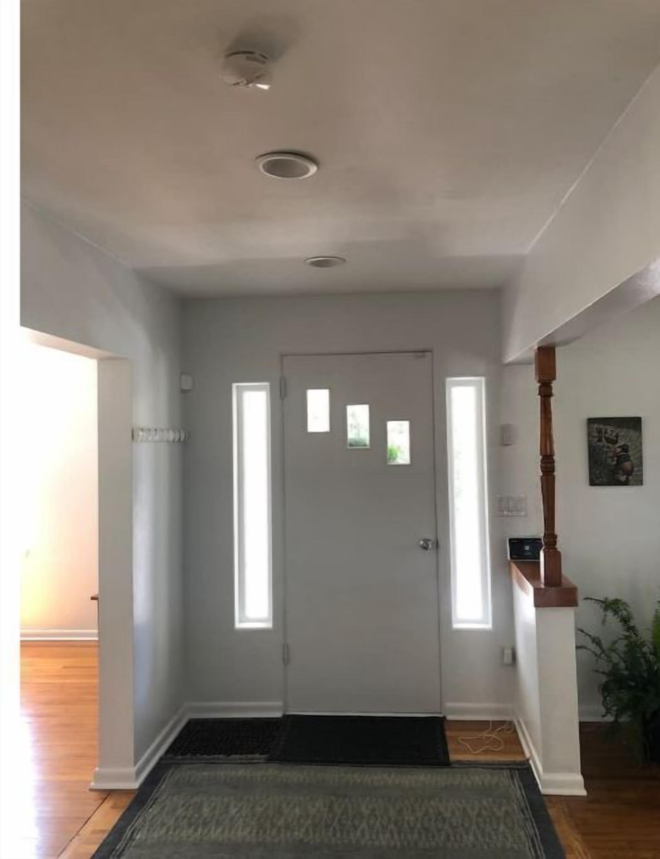 Un couloir avec une porte blanche, un escalier en bois et une petite fenêtre.