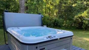 Un bain à remous sur une terrasse en bois, entouré de verdure.