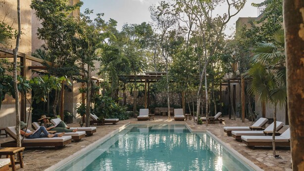 Ein Poolbereich mit Liegestühlen und einer Pergola, umgeben von Bäumen.