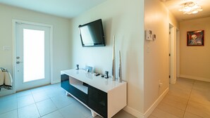 A modern bathroom with a white vanity, a mounted TV, and a door leading to another room.
