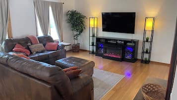 A living room with a leather sofa, a flat-screen TV, a fireplace with blue lighting, and a potted plant.