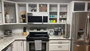 Una cocina con armarios blancos, un refrigerador de acero inoxidable, un microondas, una estufa y una cafetera.