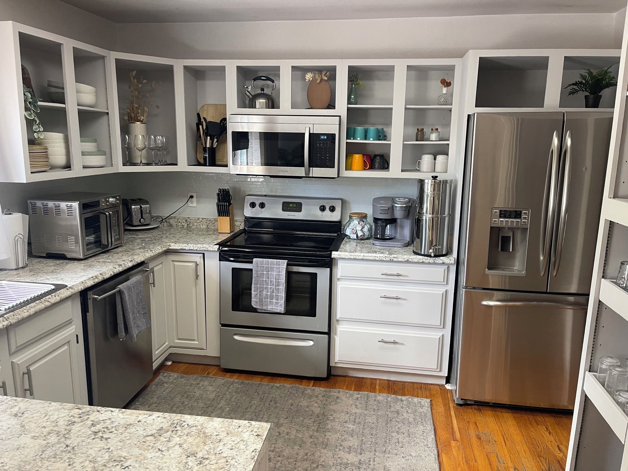 A modern kitchen with stainless steel appliances, white cabinetry, and a granite countertop.