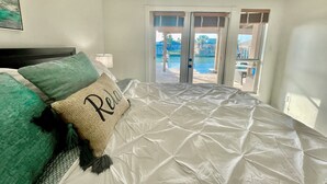 A bedroom with a bed, a pillow with 'Relax' written on it, a nightstand with a lamp, and a view of a pool and outdoor area through a sliding glass door. - Spectacular Sunsets! Private Pool & Spa on Canal - Walk to Beach & Restaurants!! (Corpus Christi)