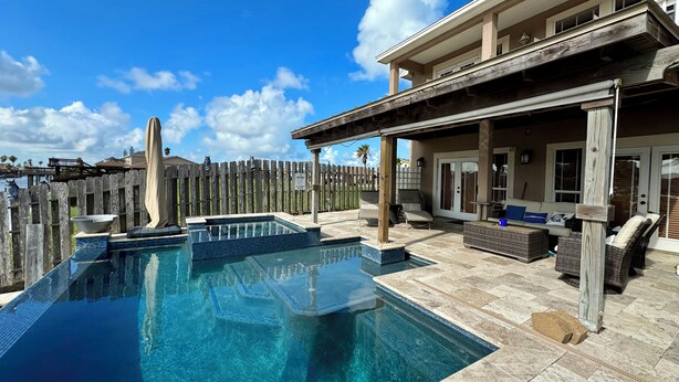 A swimming pool with a wooden deck and lounge chairs, a covered patio area, and a view of the water. - Spectacular Sunsets! Private Pool & Spa on Canal - Walk to Beach & Restaurants!! (Corpus Christi)