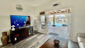 A living room with a television, a coffee table, and a sofa. There is a door leading to an outdoor area with a pool. - Spectacular Sunsets! Private Pool & Spa on Canal - Walk to Beach & Restaurants!! (Corpus Christi)