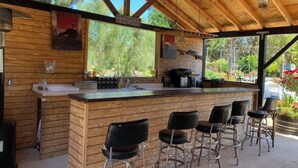 Un bar extérieur en bois, au design rustique, comprenant un comptoir et plusieurs tabourets.