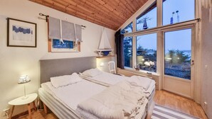 A bedroom with a large bed, a nightstand, a lamp, a window with a view of trees, and a framed picture on the wall. - Cozy home in Lidköping with WiFi (Lidköping)