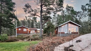 A cabin with a large glass door and a wooden exterior, surrounded by trees and a grassy area. - Cozy home in Lidköping with WiFi (Lidköping)