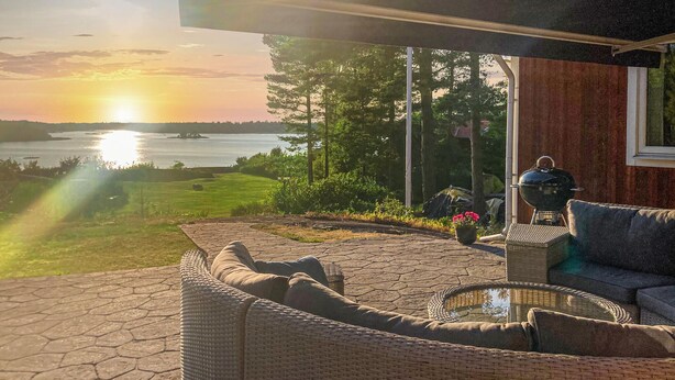 A patio with wicker furniture, a grill, and a view of a lake at sunset. - Cozy home in Lidköping with WiFi (Lidköping)