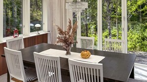 A dining area with a dark wooden table, white chairs, a clear vase with dried flowers, and a chandelier. - Cozy home in Lidköping with WiFi (Lidköping)