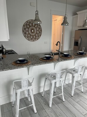 A modern kitchen with white cabinetry, a granite countertop, and a built-in bar area with white bar stools.