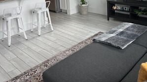 Una cocina moderna con armarios blancos, un refrigerador de acero inoxidable y una zona de comedor con taburetes blancos.