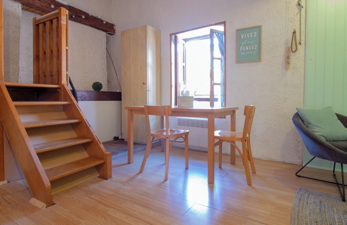 Ein Zimmer mit einer Holztreppe, einem Tisch mit zwei Stühlen, einem Fenster mit Vorhängen und einer grünen Wand.