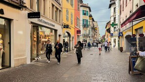 En kullerstensgata kantad av färgglada byggnader, inklusive en butik med skyltfönster där man kan se klädställ och en skylt som visar texten "Intimissimi".