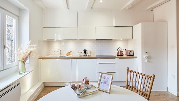 A modern kitchen with white cabinets, a wooden countertop, and a dining table with a framed certificate. - Nemours du château emplacement de rêve (Annecy)