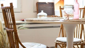 A dining table with a white tablecloth, surrounded by wicker chairs. A glass jar with a cork stopper and a white glass ornament are on the table. - Nemours du château emplacement de rêve (Annecy)