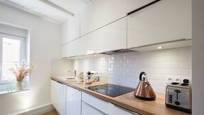 A modern kitchen with white cabinets, a wooden countertop, a kettle, a toaster, and a window with a plant. - Nemours du château emplacement de rêve (Annecy)